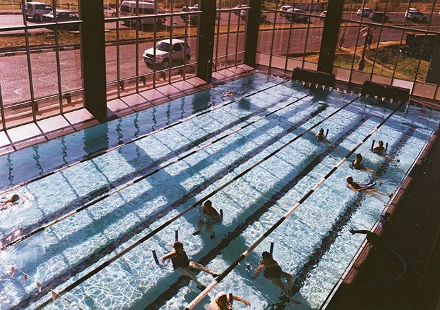 People participate in a water aerobics class in a bright indoor swimming pool, promoting fitness and healthy lifestyle.