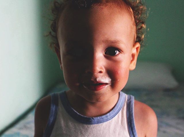 A cute toddler with milk on his face smiles at the camera in a bright room.