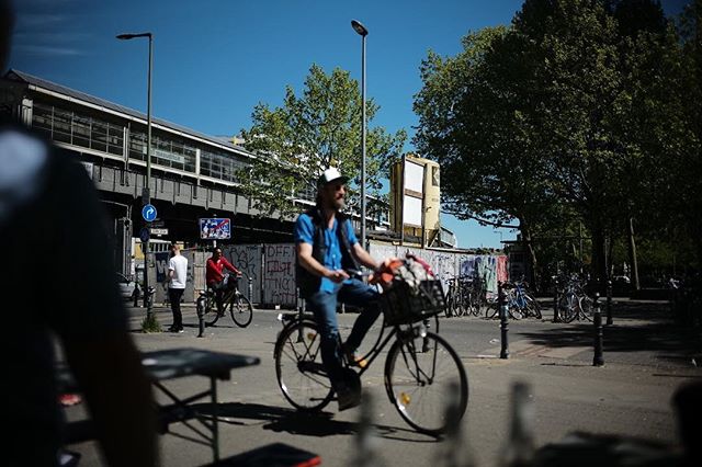 A man is riding his bicycle on a sunny city street with buildings in the background.