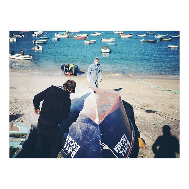 People are working on boats at the beach, with many boats visible on the water.