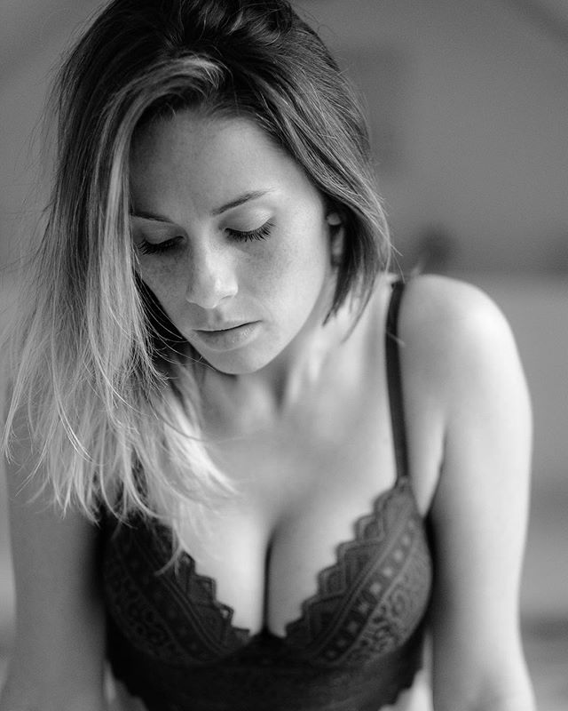 A captivating monochrome portrait of a woman with freckles in a delicate bra, eyes lowered in an intimate setting.
