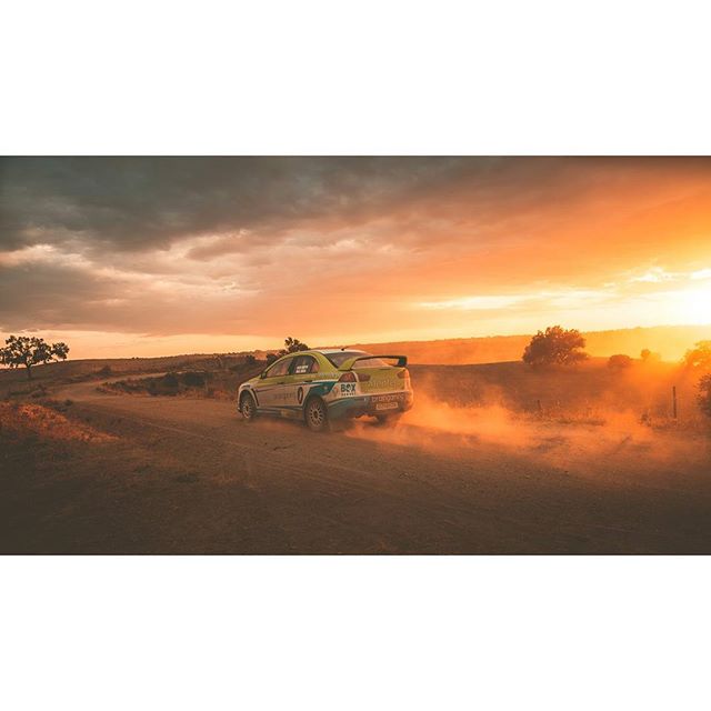 A rally car races down a dirt road amidst a vibrant sunset, capturing the thrill of motorsports and outdoor adventure.