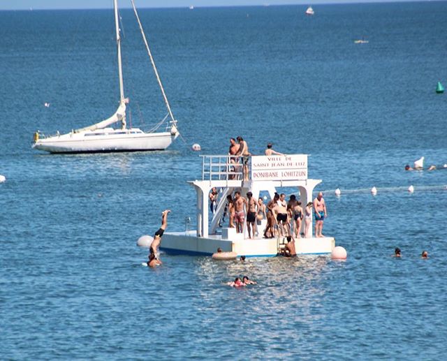 People enjoy swimming and relaxing around a boat on a sunny day at the beach, enjoying the summer weather.