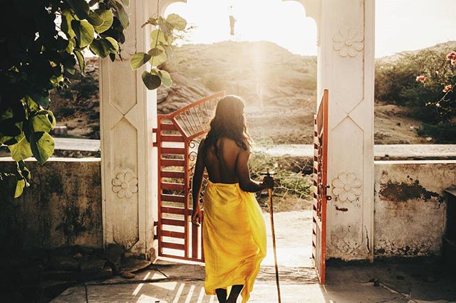 A lone figure walks through an ancient gate, bathed in sunlight, towards a tranquil landscape.