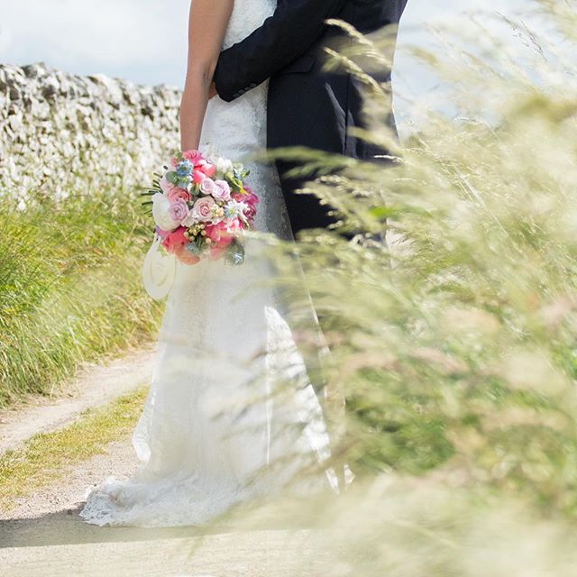 A bride and groom embrace, the bride holding a colorful bouquet on a countryside path.