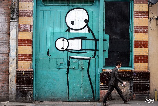 A man walks past street art depicting a stick figure carrying another figure on a building facade.