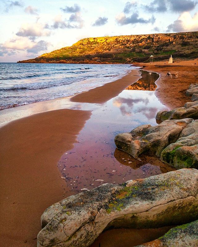 A scenic beach with rocks and reflections under a cloudy sky at sunset. Beautiful coastal landscape.