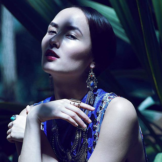A woman with jewelry poses outdoors, bathed in soft light for a sophisticated fashion editorial.