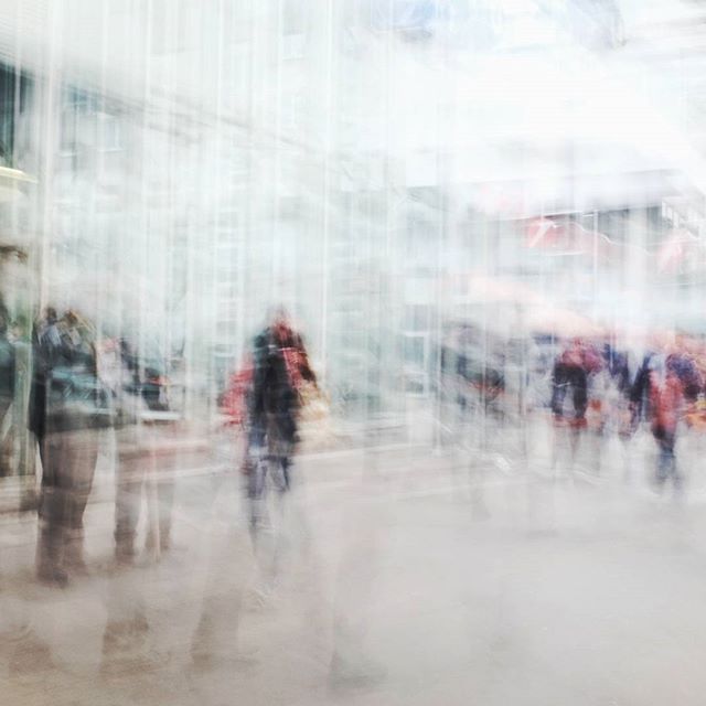 Abstract street scene featuring blurred figures in an urban setting, conveying a sense of movement and mystery.