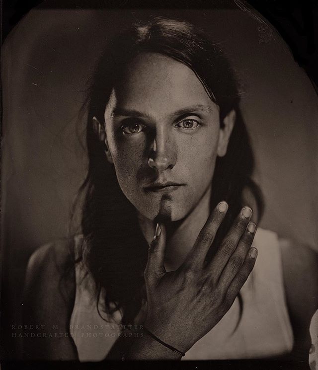 Artistic black and white portrait of a person with a hand partially obscuring their face.