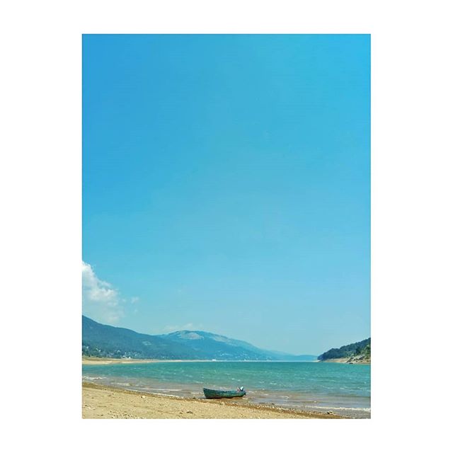A tranquil lake scene with a boat on the shore, surrounded by mountains under a clear blue sky.