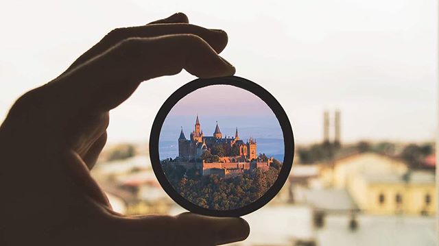 Hand holding a lens displaying a castle on a hilltop. Scenic travel destination.