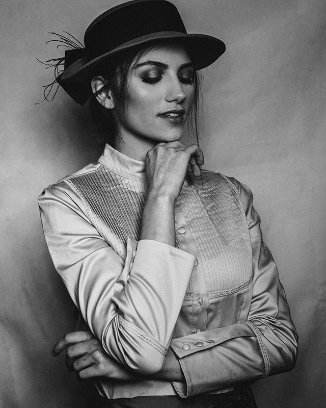 A stylish woman in a hat poses in a black and white portrait with an elegant, vintage style.