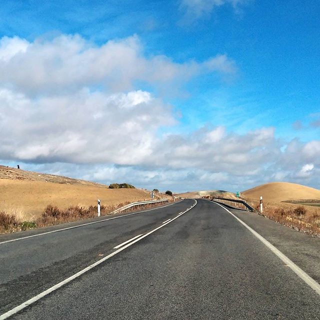 A scenic road cuts through rolling hills under a bright, cloudy sky, ideal for travel or landscape themes.
