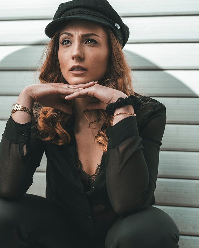 A woman wearing a hat poses thoughtfully in an outdoor setting.