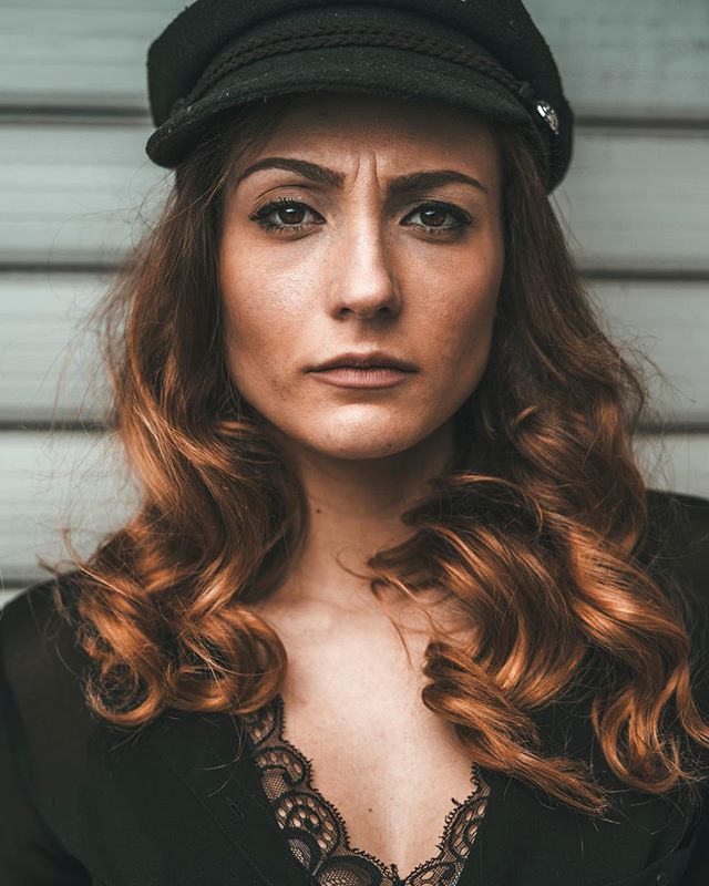 Intense portrait of a woman in a newsboy cap with soft, diffused lighting and a serious expression.