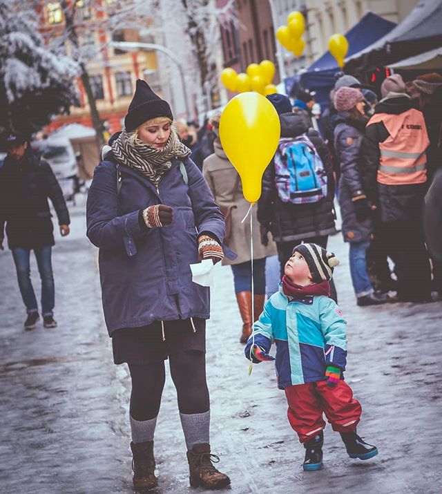 A woman and a child are walking down a street with yellow balloons.