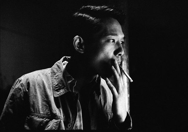 A stylish man in black and white enjoys a cigarette in a moment of contemplation.
