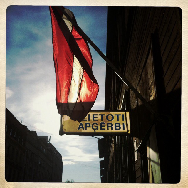 A Latvian flag hangs outside a building, creating a scene evoking city tourism and cultural heritage.
