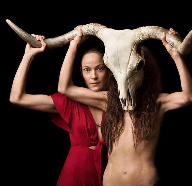 Two women pose artistically with a bull skull against a black backdrop, creating a mysterious and powerful image.