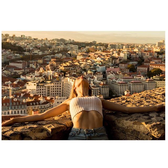 A woman stretches her arms out on a stone ledge with a city view in the background.