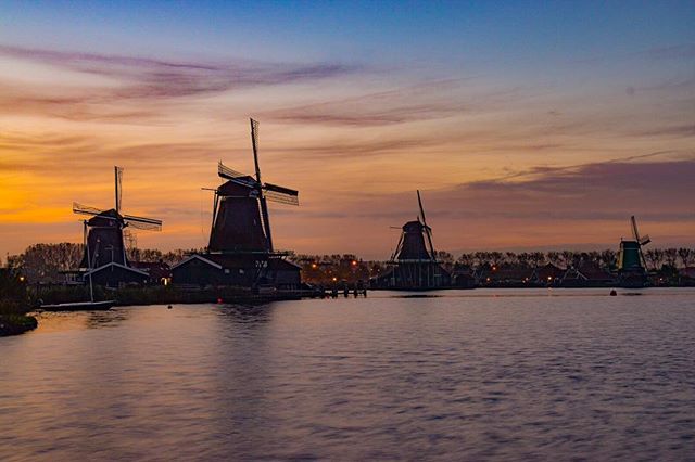 Windmills at Zaanse Schans, Netherlands, during a tranquil sunset with warm colors reflecting in the water.