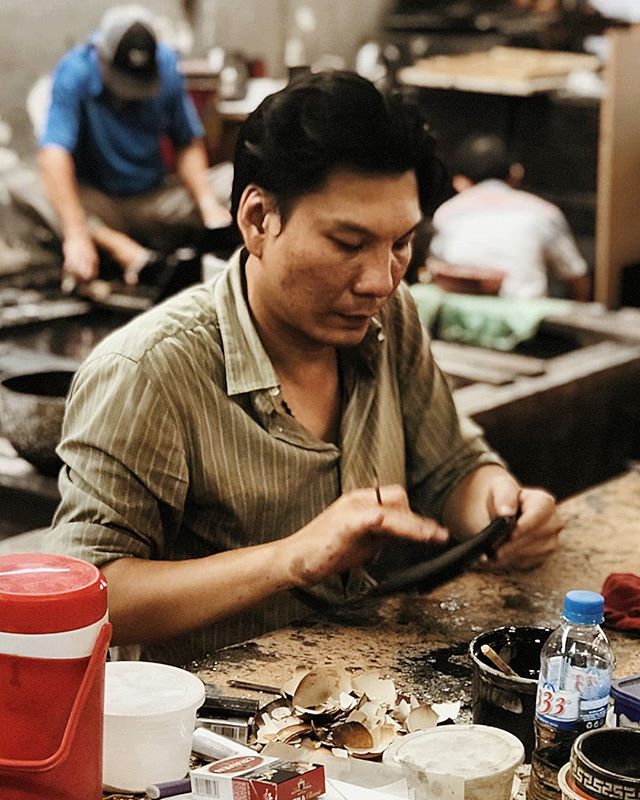 A craftsman focuses on his leatherwork at his table in a workshop, surrounded by tools.