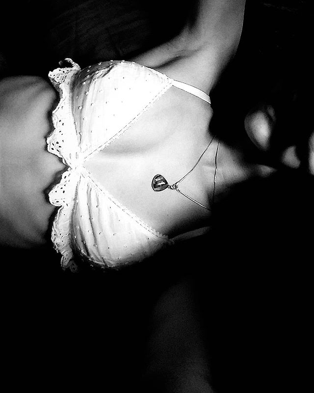 An artistic black and white image of a woman with a necklace, wearing a bra.