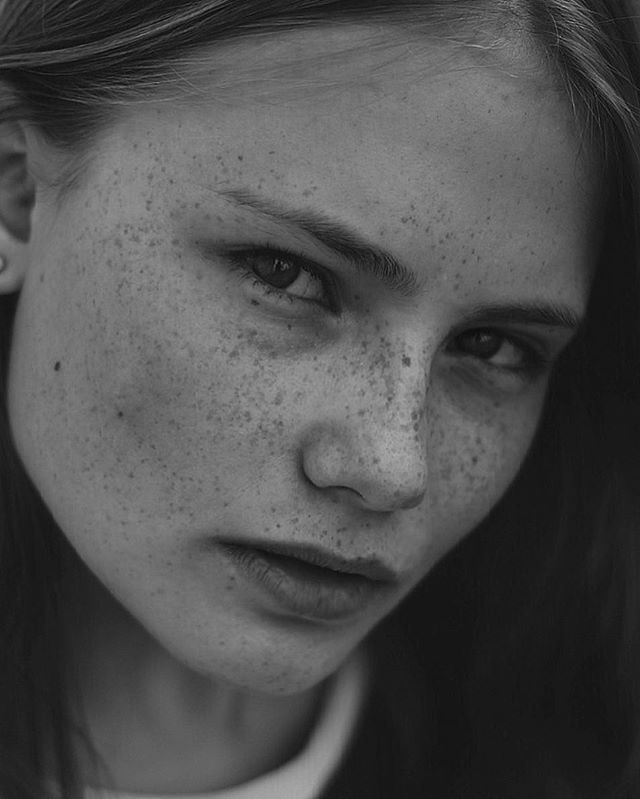 A close-up black and white portrait of a woman with freckles in an editorial style.