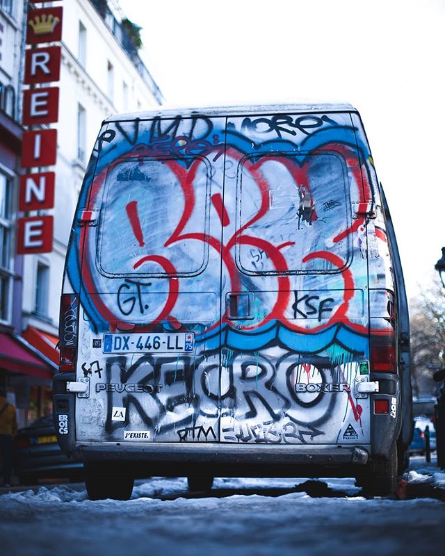 A graffiti-covered Peugeot van is parked on a city street with a weathered, artistic vibe.