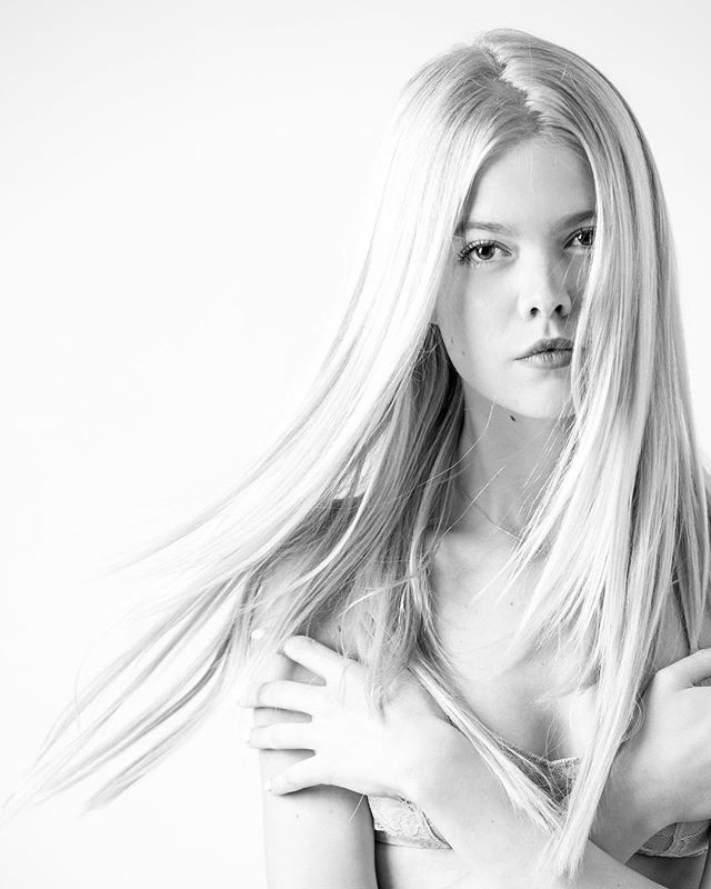 Striking black and white portrait of a young woman with blonde hair in a minimalist studio setting.