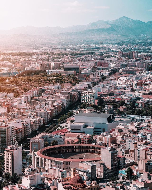 A captivating aerial view shows a cityscape with buildings, a bullring, and mountains in the background.