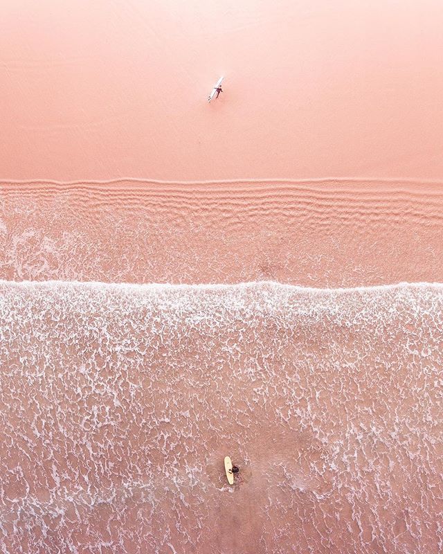 Aerial view of a pink sand beach with surfers in the ocean.