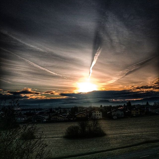 A scenic landscape capturing the sunrise over a quaint town, with dramatic clouds filling the sky.