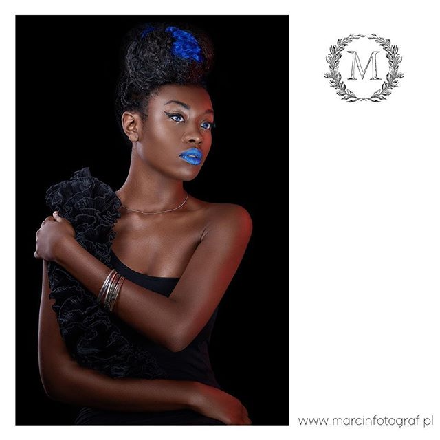 Elegant model with blue makeup poses in a studio with a black background for a fashion editorial.