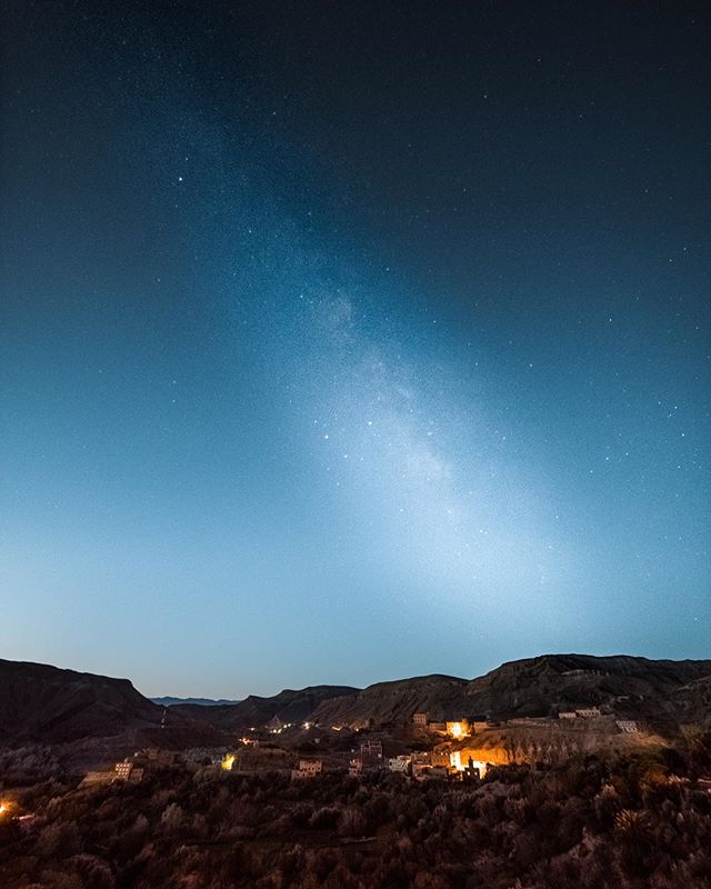 A tranquil night landscape of a village nestled in the mountains under a starry Milky Way sky.