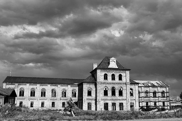 An old abandoned building with dramatic sky is shown in black and white.