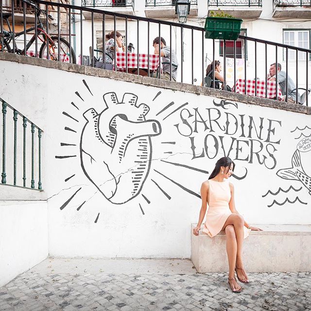 A woman in a dress sits in front of a mural at an outdoor cafe.