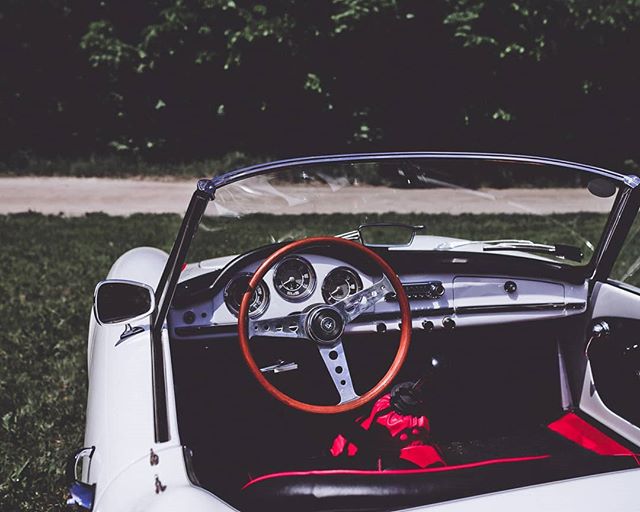Interior view of a classic white convertible with a wooden steering wheel on a grassy roadside setting.