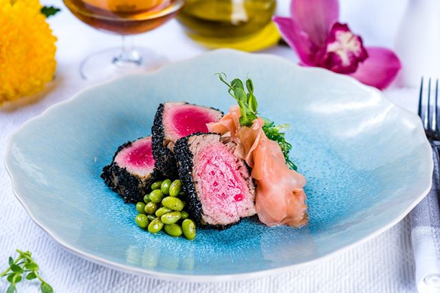 A gourmet tuna steak plated with edamame and ginger, presented in a modern restaurant setting.