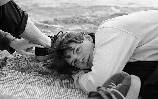A woman lies on a checkered blanket at the beach in a thoughtful and tranquil mood.