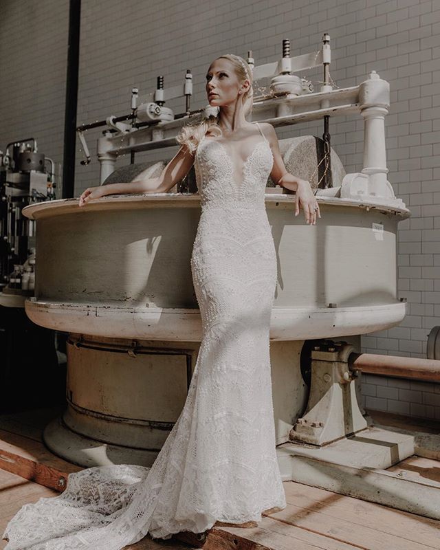 A bride in a lace wedding dress poses in an industrial setting for a bridal fashion editorial.