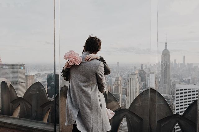 A couple embraces on a rooftop overlooking the New York City skyline and the Empire State Building.