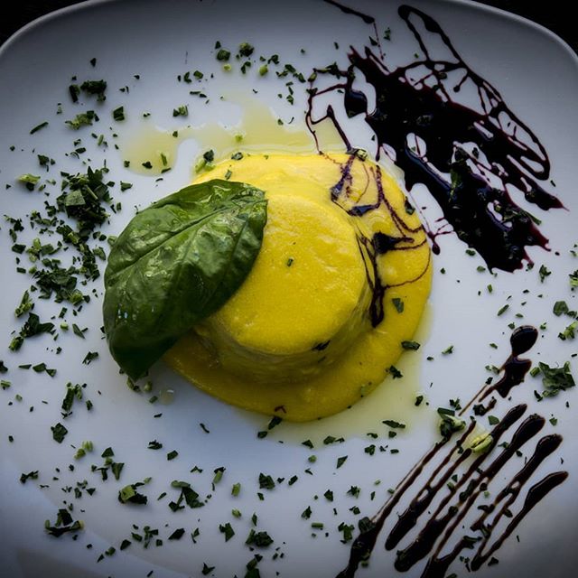 A vibrant polenta dessert is plated with fresh basil and balsamic glaze on a white plate.