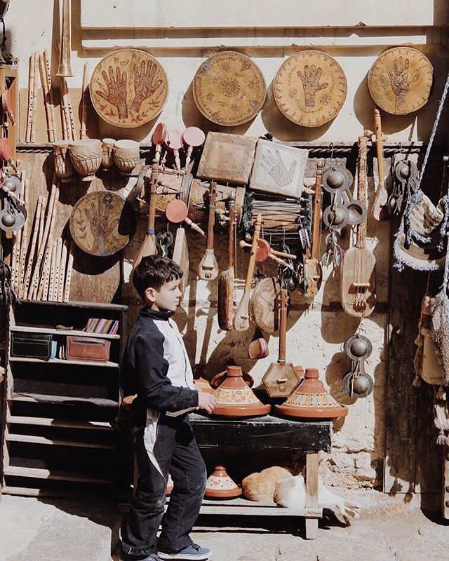 A boy stands in front of a shop displaying traditional musical instruments and crafts, with a cat sleeping nearby.