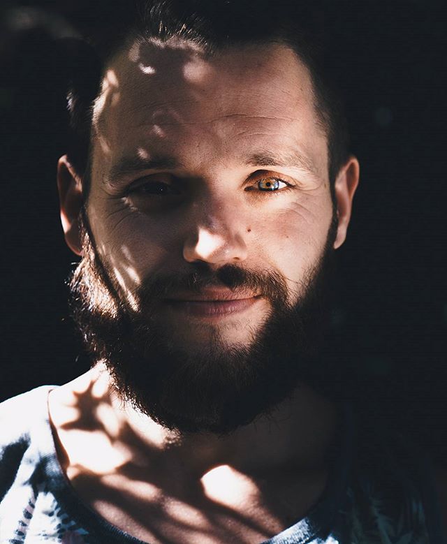 A bearded man's intense portrait, with shadows creating a moody and artistic effect. 