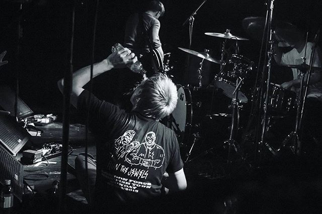 A black and white shot captures a band performing intensely on stage, a man pouring water over himself.