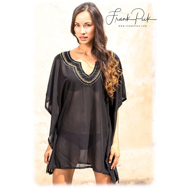 A woman poses in a black beach coverup, showcasing summer fashion and relaxed vacation style.