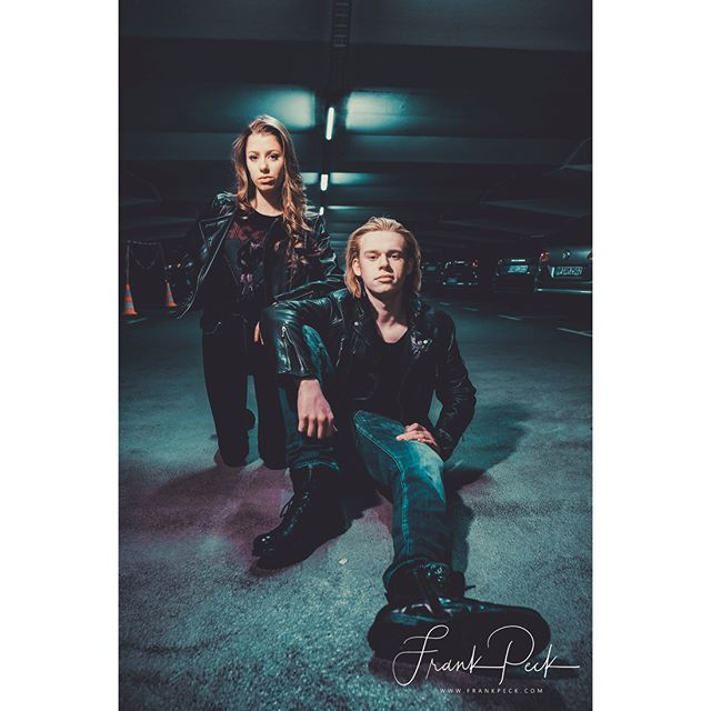 A stylish couple in leather jackets poses in an urban parking garage for a modern fashion shoot.