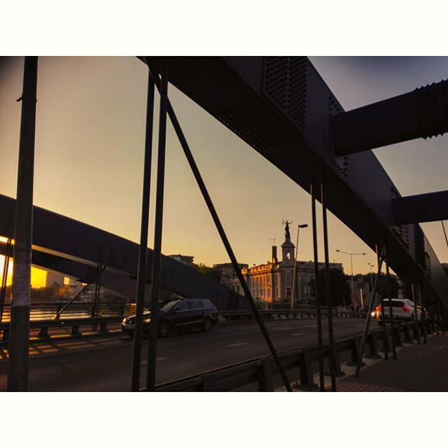 A bridge with cars and a statue is captured at sunset, creating a serene and urban landscape.